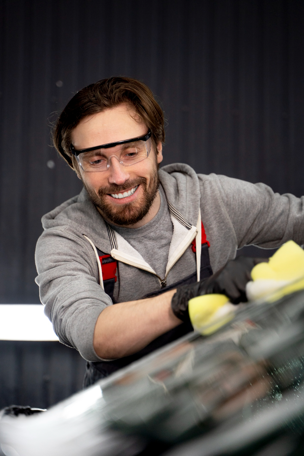 Technicien express souriant nettoyant une vitre avec soin en atelier auto dans le Tarn-et-Garonne